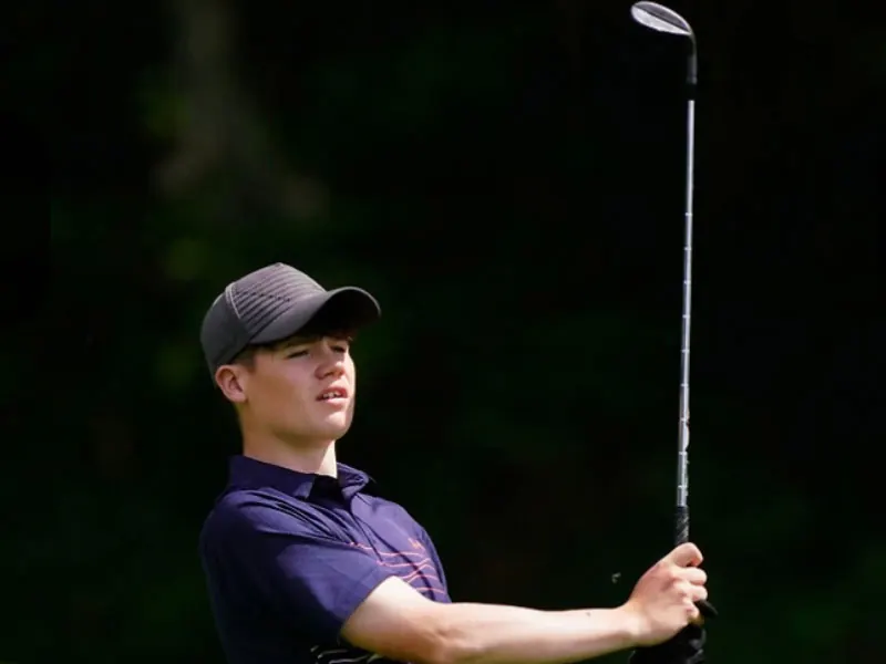 Young golfer Adam Buchanan mid-swing, watching his shot with the club raised