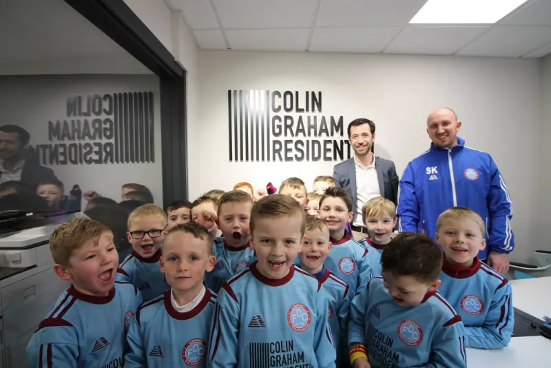 Carnmoney FDC youngsters in their sponsored kits in front of the Colin Graham Residential sign