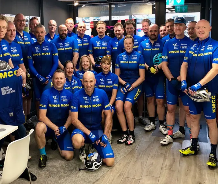 A large group of Kings Moss Cycling Club members in blue club kit gathered indoors before a ride